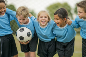 A multi-ethnic group of elementary age children are standing together before their soccer game. One girl is smiling and looking at the camera.