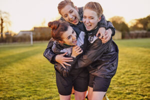 Group of three female footballers embracing in celebration after match in warm evening light