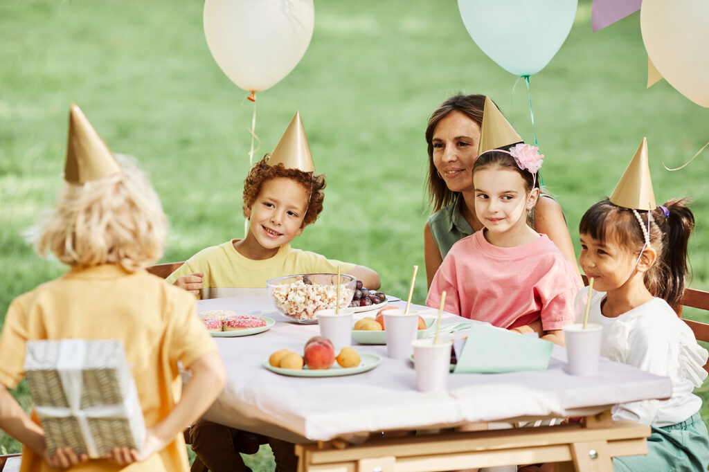 Back view at little boy hiding gift during outdoor Birthday party in Summer