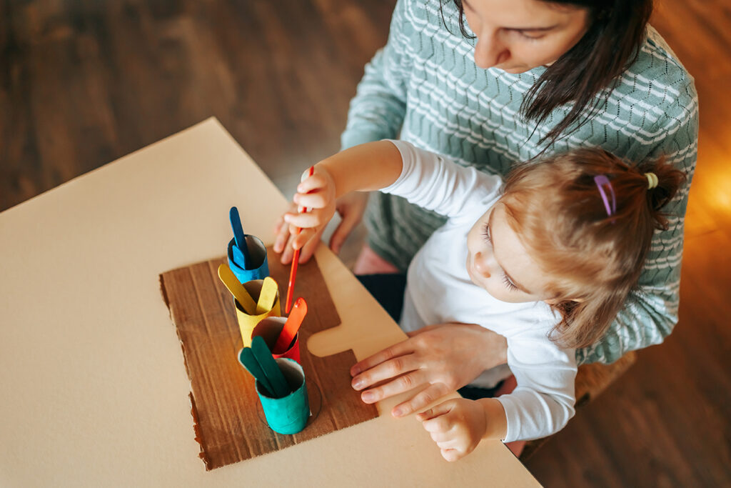 Top view of a young woman with a little girl doing children activities, interesting educational games. workplace. Educational games for children concept.